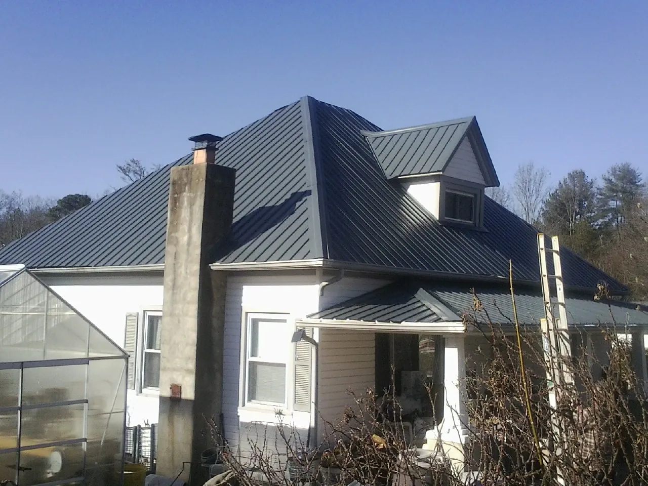 Dark blue standing seam metal roof on a white farmhouse with dormer — Slate & Tile Roof Repair by Roofing Brothers in Calamus