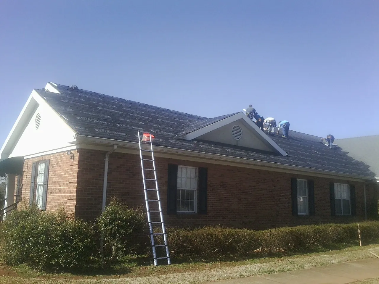 Crew tearing shingles off a brick ranch roof with a ladder set — Emergency Roof Repair work by our crew in Calamus