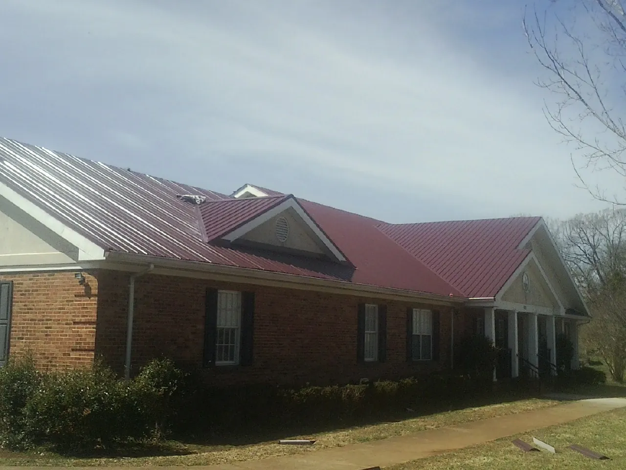 Red metal roof with gabled entries on a long brick building, from a Hail Damage Roof Repair job in Calamus