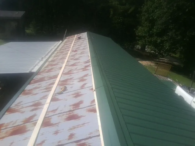 Old rusted panels beside newly installed green metal roofing — Wind Damage Roof Repair by Roofing Brothers in Calamus