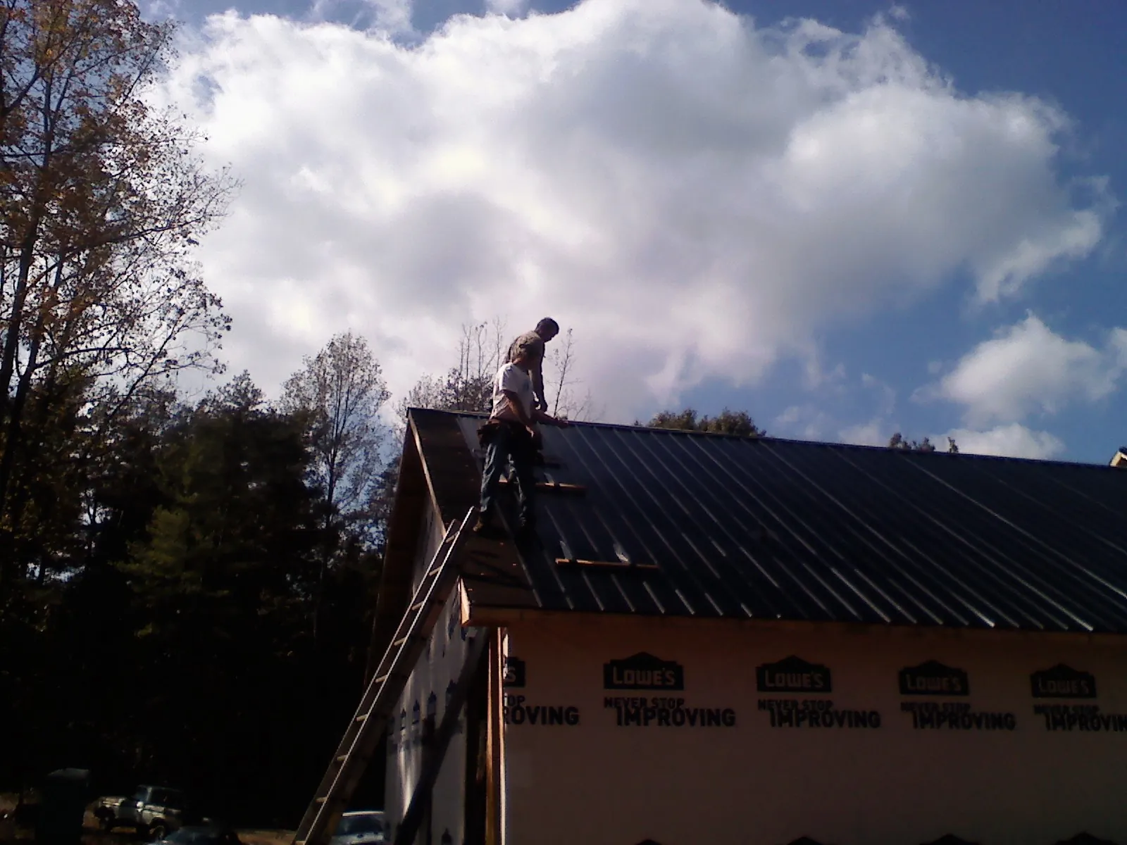 Roofer fastening dark metal panels high against a cloudy sky, from a Roof Inspection job in Calamus