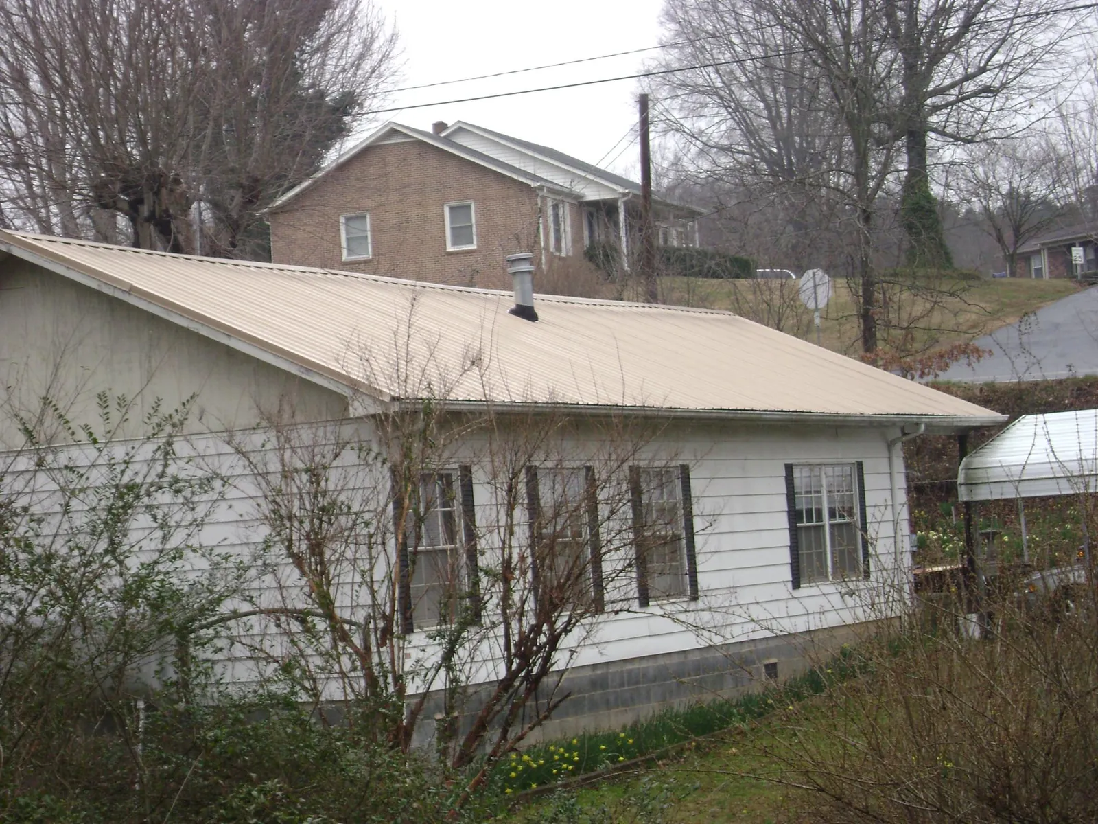 Tan metal roof on a white sided house set into a hillside — Commercial Roofing by Roofing Brothers in Calamus