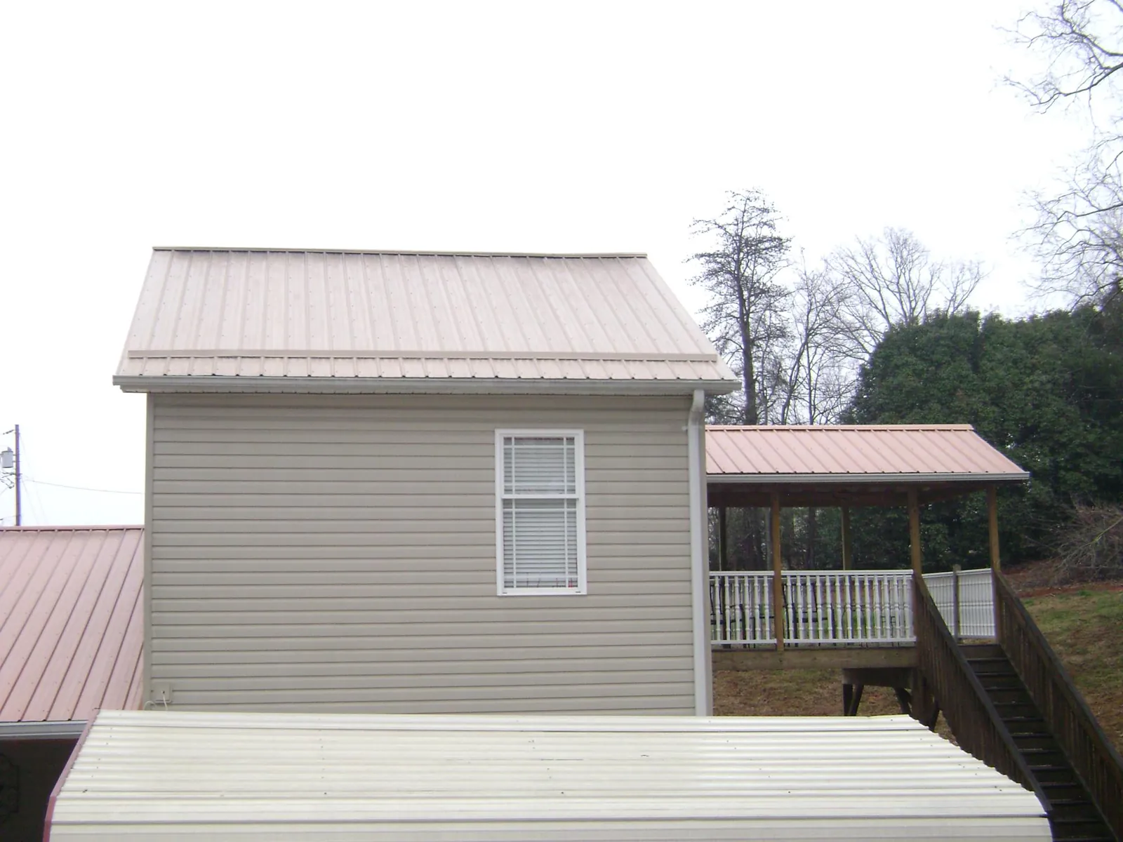 Tan metal roofs on a two story addition and attached porch, from a Roof Replacement job in Calamus